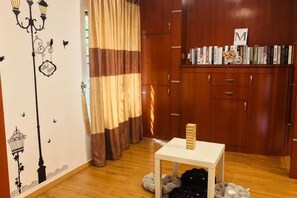 A room with a wooden floor, a white table with a basket, a bookshelf with books, and a curtain with a striped pattern.