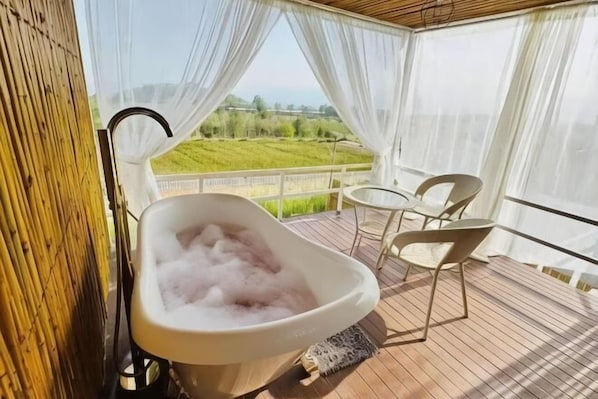 Un balcon avec une baignoire, des chaises et une vue sur un paysage verdoyant.