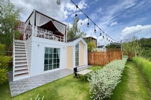 Ein zweistöckiges Haus mit einem Balkon, einer Terrasse mit Tisch und Stühlen und einem gepflegten Garten.