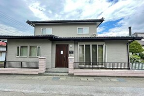 A two-story residential building with a front entrance, a small porch, and a garage. - YiyashiHikari Fujiyoshida No.1 (Fujiyoshida)