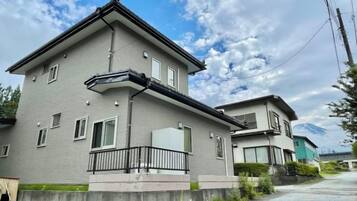 A two-story residential building with a balcony, a garage, and a visible mountain in the background.