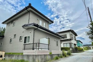 A two-story residential building with a balcony, a garage, and a visible mountain in the background. - YiyashiHikari Fujiyoshida No.1 (Fujiyoshida)