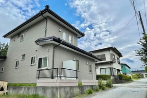 Un edificio residencial de dos pisos con un balcón, un garaje y una montaña visible al fondo.