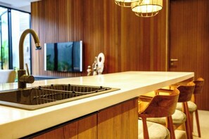 A modern kitchen with a large island, stainless steel sink, wooden cabinetry, and bar stools. - Casa Tropicale Seminyak (Bali)