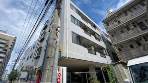 A multi-story building with a flat facade, balconies, and a sign indicating a business or service on the ground floor. - Nagomi An (Tokyo)
