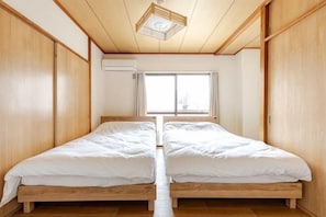 Ein Zimmer mit zwei Betten, Holzboden, einem fenster mit Vorhängen und einer Deckenleuchte.