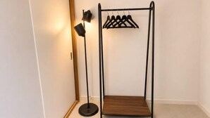 A corner of a room with a black metal coat rack holding several hangers, a black floor lamp, and a wooden bench. - Nagomi An (Tokyo)