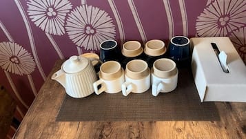 A table with a teapot, six cups, and a tissue box.