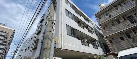 Un edificio de varios pisos con fachada plana, varios balcones y una entrada visible.