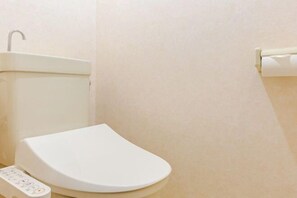 A bathroom with a white toilet, a wall-mounted sink, and a toilet paper holder. - Nagomi An (Tokyo)