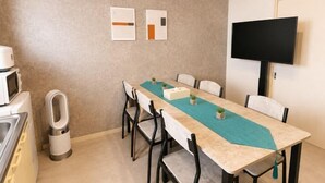 A dining area with a long table, chairs, a microwave, and a TV mounted on the wall. - Nagomi An (Tokyo)