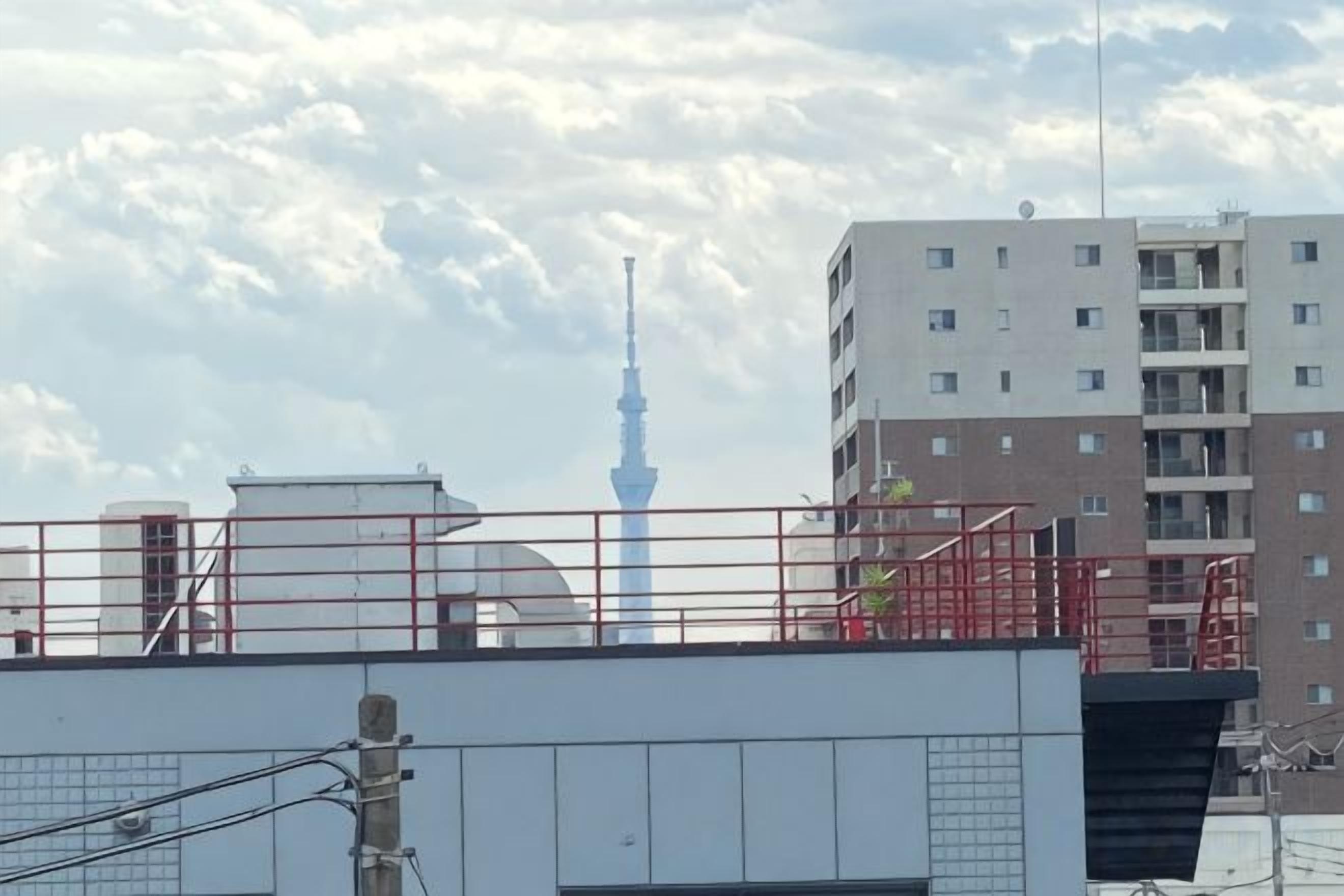 A building with a flat roof, a red railing, and a tower in the background.