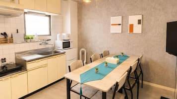 A compact kitchen with a dining area, a microwave, and a flat-screen TV mounted on the wall.