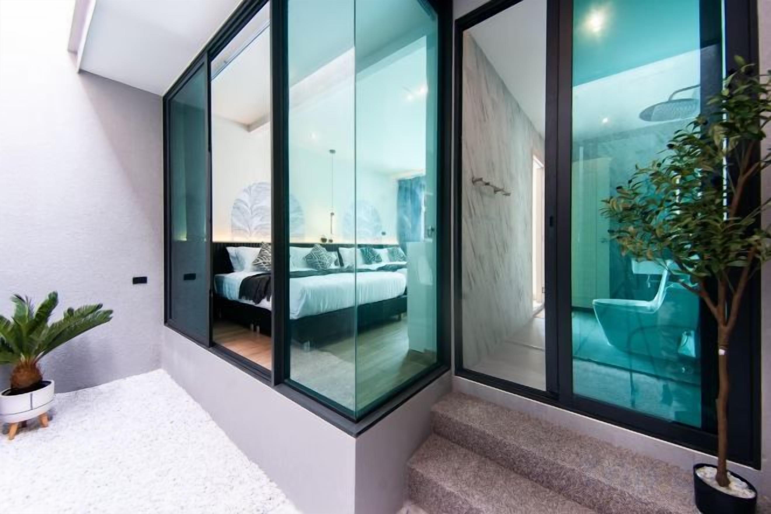 A modern hotel room with a glass partition, a bed, a potted plant, and a staircase.