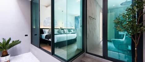 A modern hotel room with a glass partition, a bed, a potted plant, and a staircase.