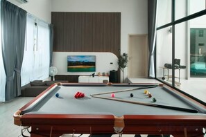 A pool table in a modern room with a large window, a flat-screen TV, and a sofa. - Nacha Pool Villa Cha-am (Cha-am)