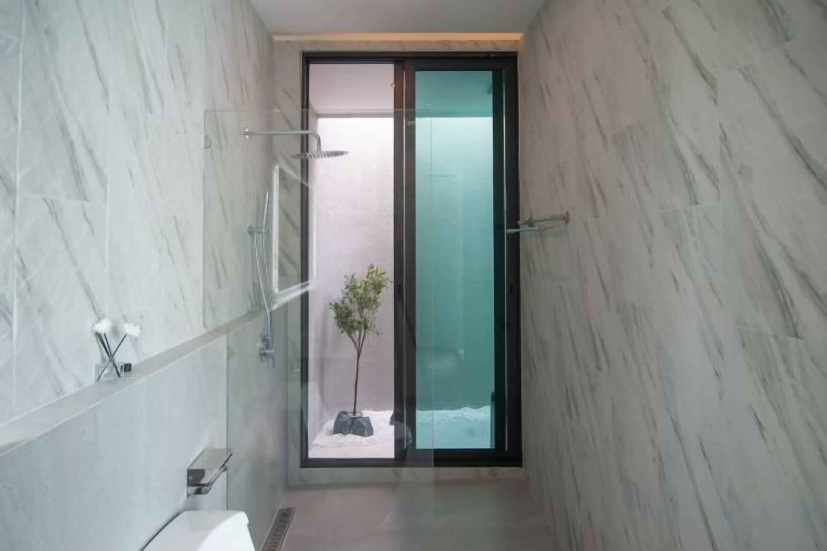 A modern bathroom with a glass shower enclosure, a small plant, and a marble wall.