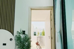 A room with a large window, a potted plant, and a door leading to an outdoor balcony. - Nacha Pool Villa Cha-am (Cha-am)