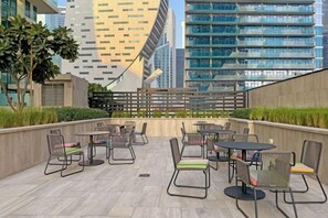 An outdoor seating area with tables and chairs, surrounded by a low wall and greenery, with modern buildings in the background. - bnbme Luxurious Canal View Apt w/ Pool & Gym (Dubai)