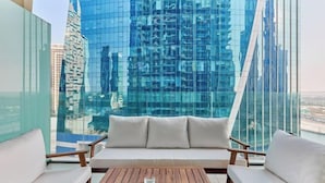 Un balcon aménagé avec un canapé et deux fauteuils, offrant une vue sur le paysage urbain et ses bâtiments modernes.