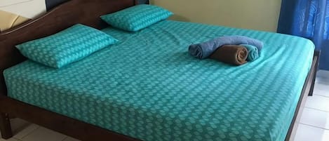 A bed with a patterned bedspread, two pillows, and a rolled towel.
