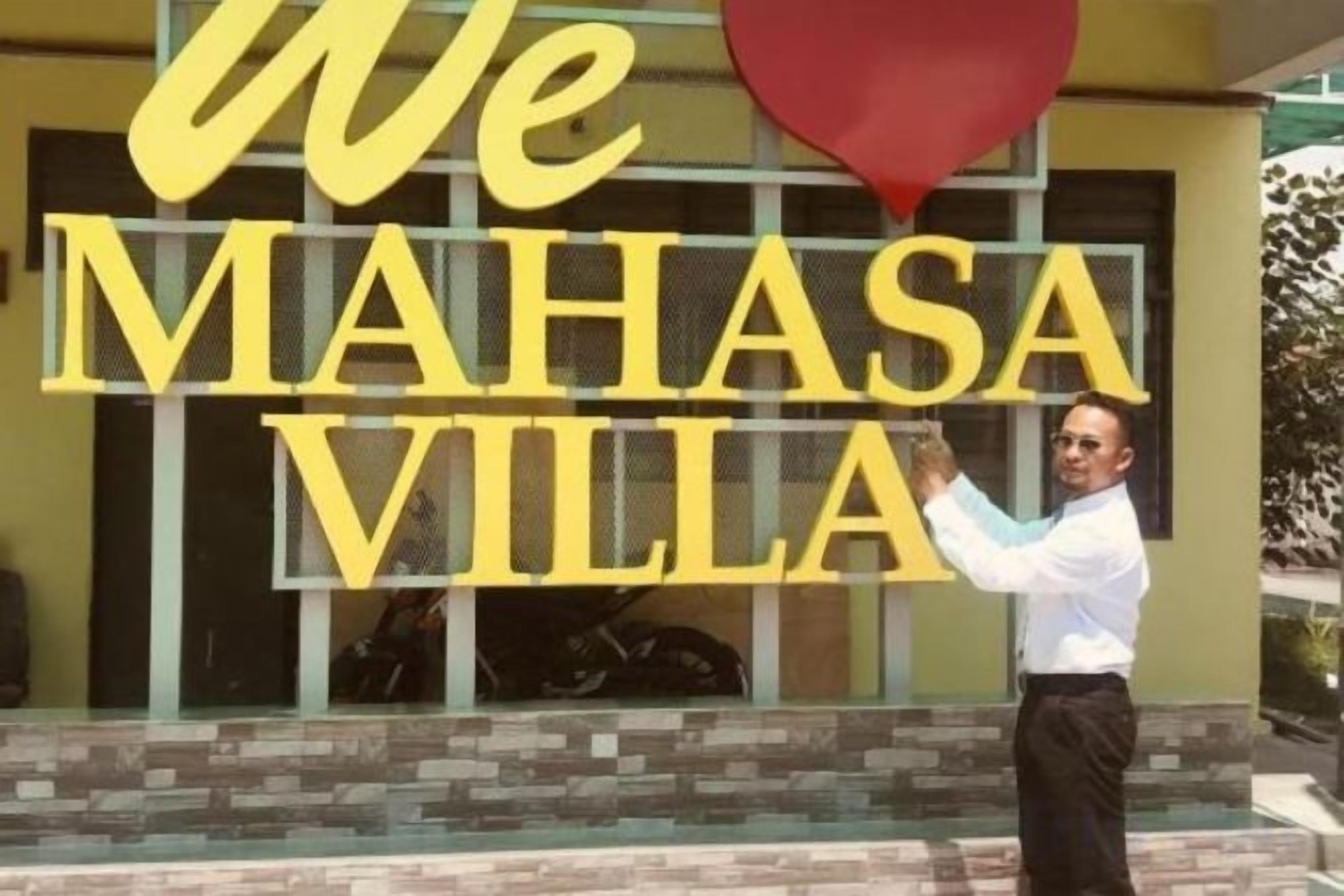 Una persona está de pie frente a un edificio con letras amarillas grandes que deletrean 'We Mahasa Villa'.