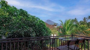 A balcony with a table and chairs, surrounded by lush greenery and a mountain in the background. - Sekarini Place Amed (Bali)