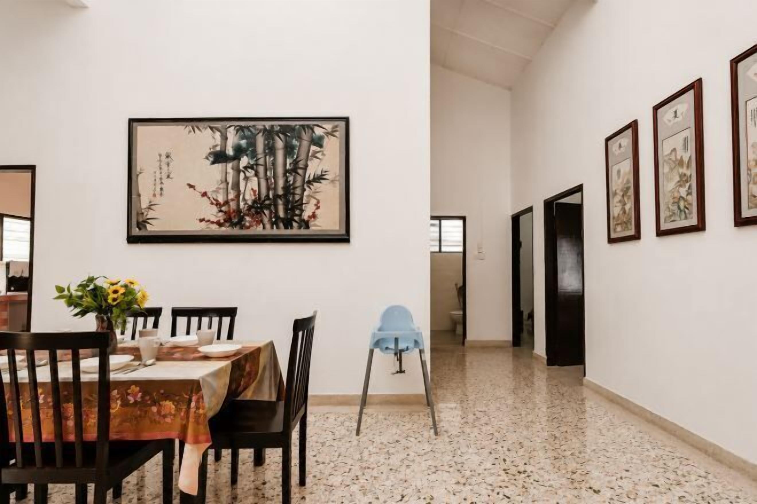 A dining area with a table set for four, chairs, a vase with flowers, and framed artwork on the wall.