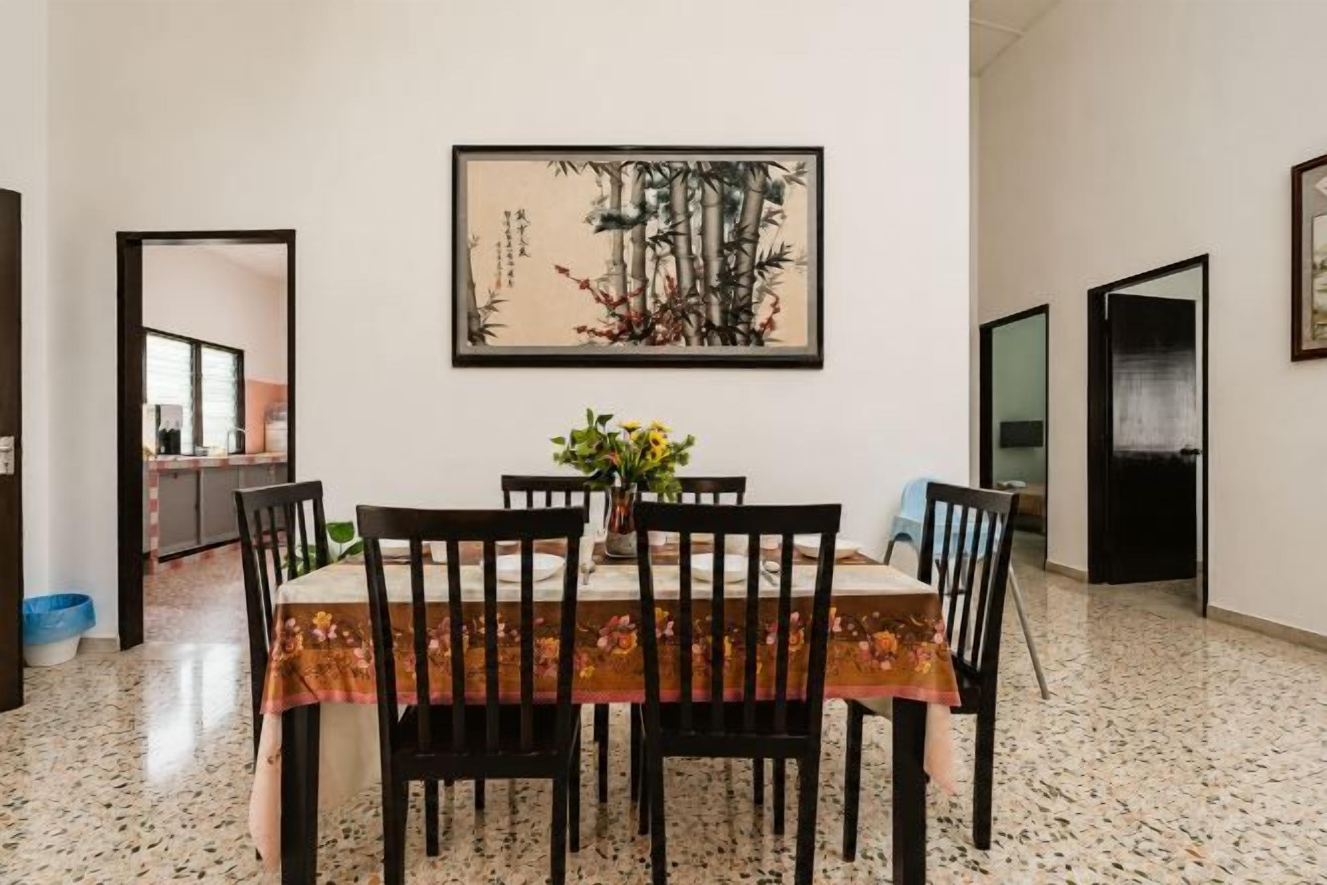 A dining area with a table set for four, a vase with flowers, and a painting on the wall.