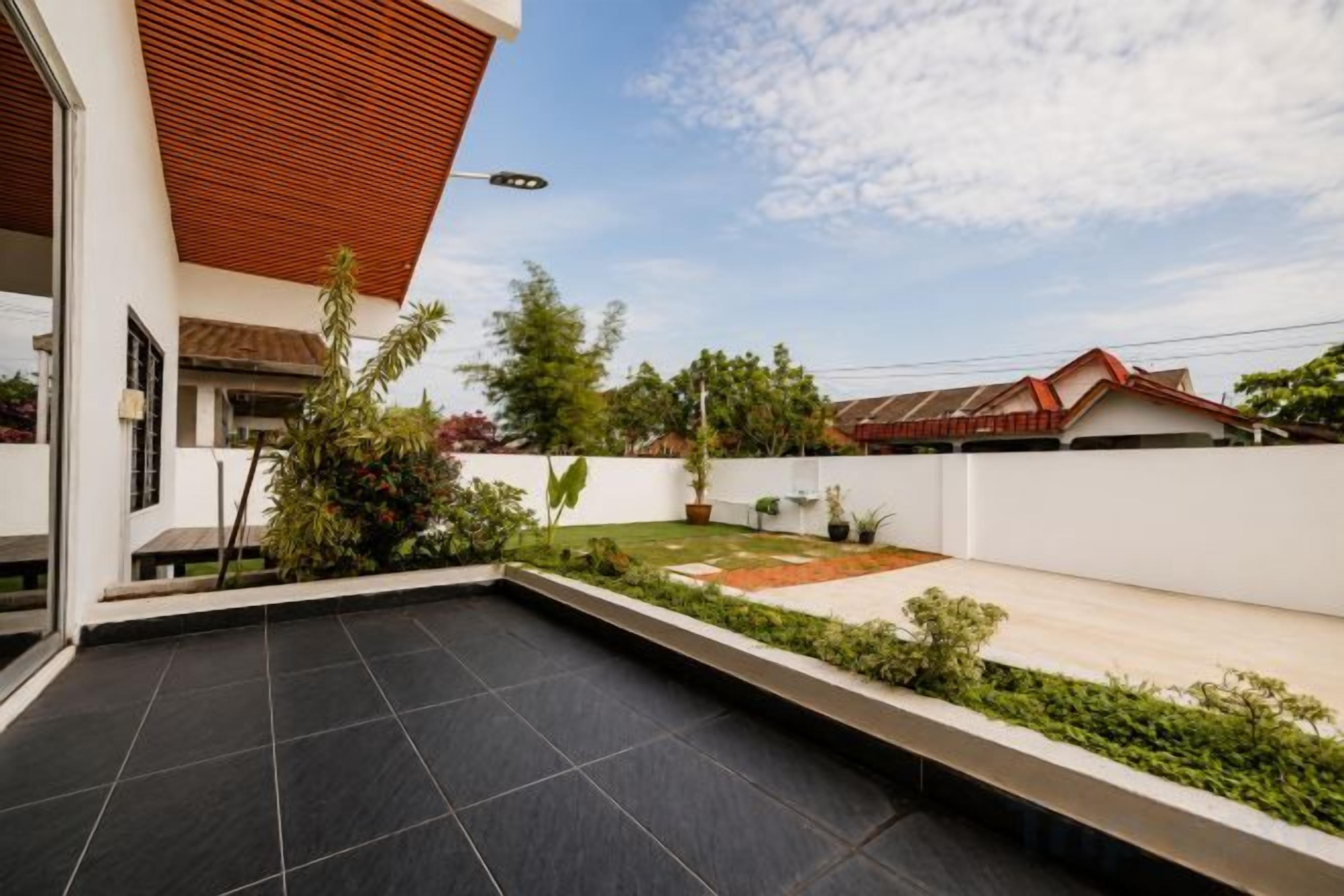 A modern outdoor patio area with a flat surface, surrounded by a low white wall, and a wooden ceiling structure.