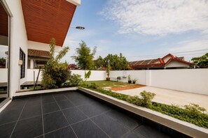 Un patio moderno al aire libre con superficie plana, rodeado por un muro blanco bajo y una estructura de techo de madera.