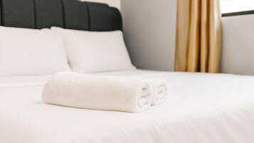 A neatly made bed with white bedding and a folded white towel.