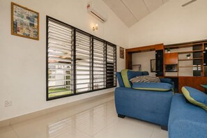 A living room with a blue sofa, a large window with blinds, and a wall-mounted air conditioner. - Batu Pahat w Pooltable Villa 4Br16Pax by Our Stay (Simpang Kanan)