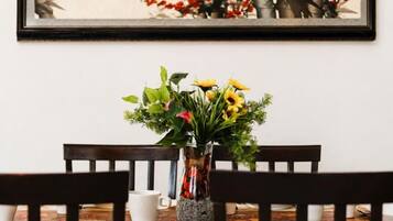Una mesa de comedor con sillas, un florero con flores y un cuadro en la pared.