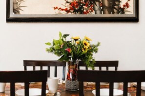 Une table à manger avec des chaises, un vase rempli de fleurs et un tableau encadré accroché au mur.