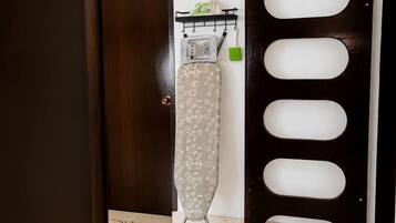 An ironing board with an iron and a green cloth in a room with a wooden door and a wall-mounted rack.