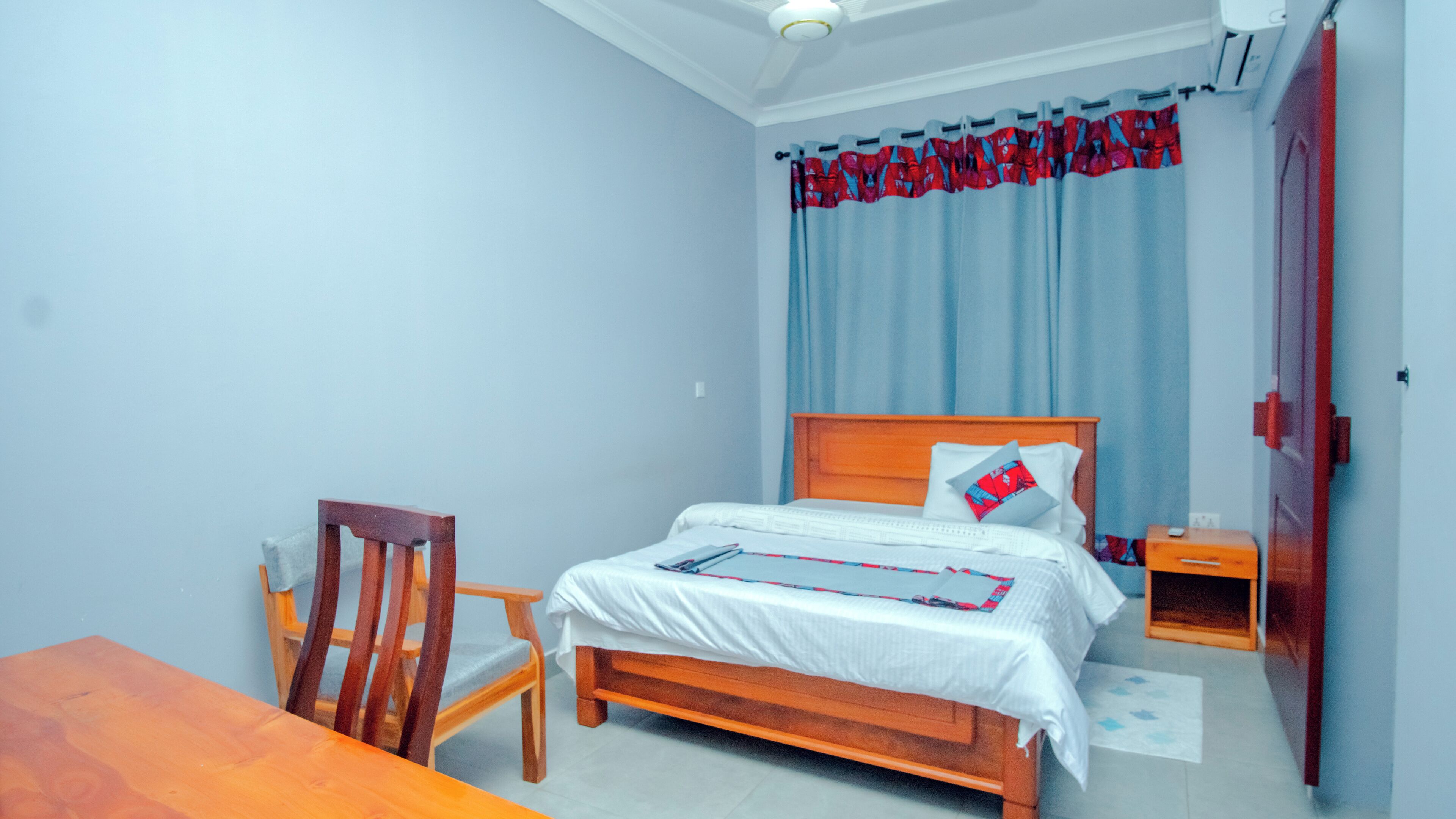 Un dormitorio con una cama de madera, una silla de madera, una mesita y un armario.