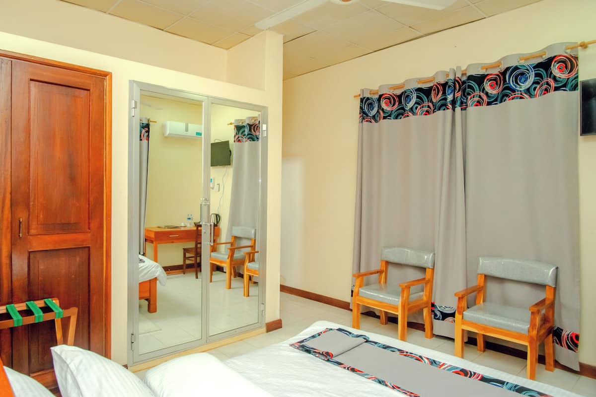 Hotellihuone, jossa on sänky, kaksi puutuolia, työpöytä tuolilla, vaatekaappi ja peili.