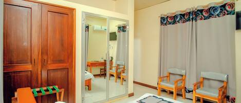 A hotel room with a bed, two wooden chairs, a desk with a chair, a wardrobe, and a mirror.