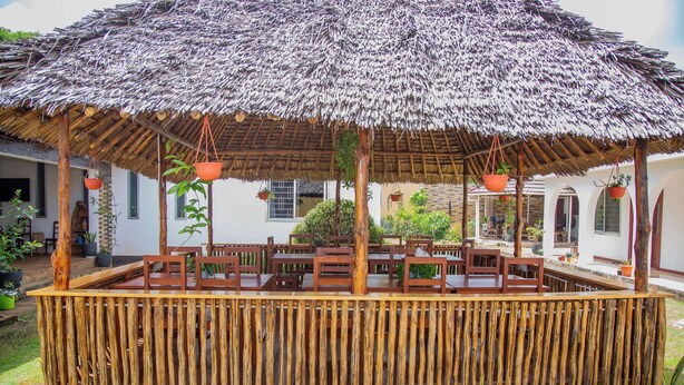 A thatched-roof outdoor seating area with wooden furniture and hanging planters.