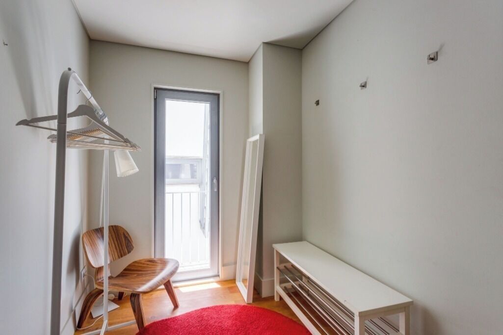 Una habitación pequeña y luminosa con una silla de madera, un banco y un perchero.