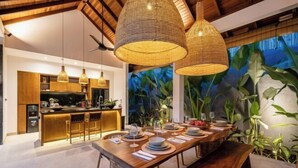 A modern kitchen with a bar area, wooden dining table, and hanging wicker lamps. - Villa Le Lotus Bleu by BaliSuperHost (Bali)