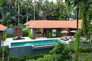 A poolside area with a house, outdoor seating, and lush greenery. - Villa Le Lotus Bleu by BaliSuperHost (Bali)