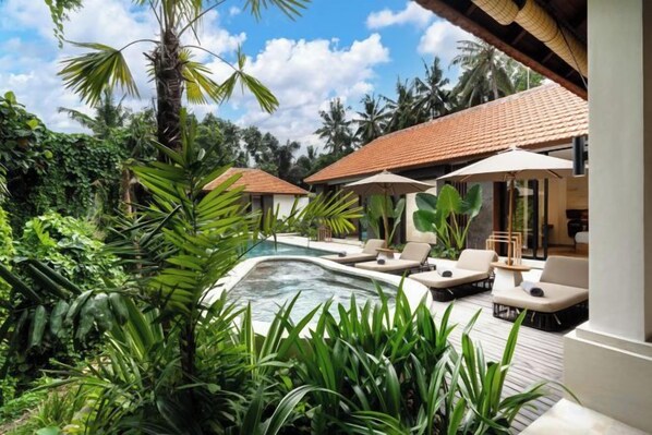 A pool area with lounge chairs and umbrellas, surrounded by lush greenery and a clear sky. - Villa Le Lotus Bleu by BaliSuperHost (Bali)