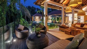 A modern outdoor lounge area with wicker furniture, a glass balustrade, and a pool in the background. - Villa Le Lotus Bleu by BaliSuperHost (Bali)