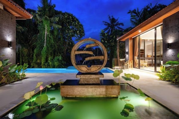 A modern outdoor pool area with a unique spherical sculpture, surrounded by lush greenery and a well-lit patio. - Villa Le Lotus Bleu by BaliSuperHost (Bali)