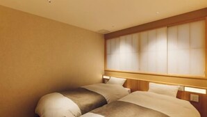 Habitació d'hotel amb dos llits, un capçal de llit de fusta i un gran finestral amb persianes.