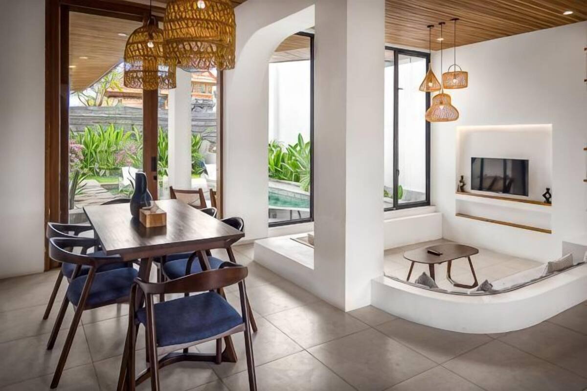 A modern dining area with a wooden table and chairs, a built-in TV, and a seating area with a small table and cushions.