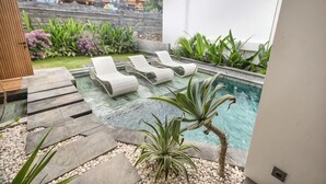 Un área de piscina con sillas de descanso, un sendero de piedra y una pequeña fuente.