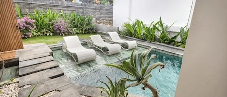 A pool area with lounge chairs, a stone pathway, and a small water feature.